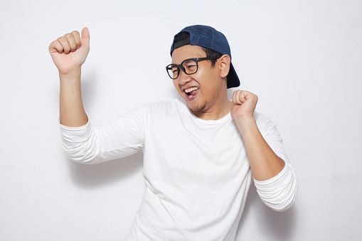 Photo image closeup portrait of a funny young Asian man dancing happily joyful expressing celebrating good news victory winning success gesture, smiling positive excited emotion while standing over white background