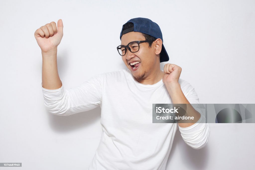 Happy Funny Asian Man Dancing Full of Joy Photo image closeup portrait of a funny young Asian man dancing happily joyful expressing celebrating good news victory winning success gesture, smiling positive excited emotion while standing over white background Men Stock Photo