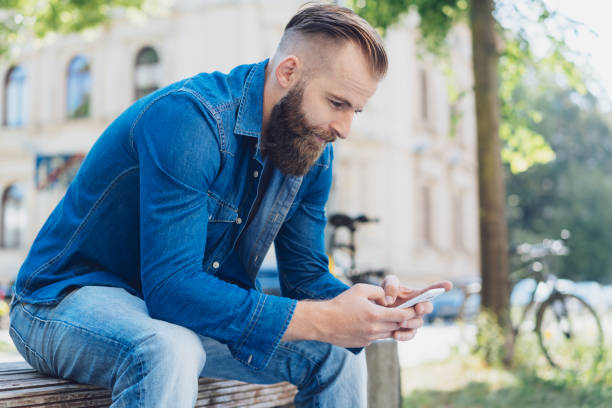 istock Casual man sitting on an urban bench texting 1076683342