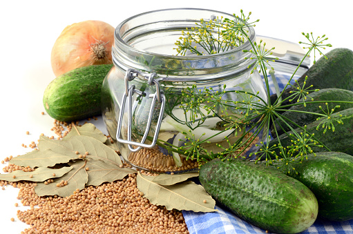 raw cucumbers in jar glass with herbs like laurel leaves, chili pepper, onions, dill