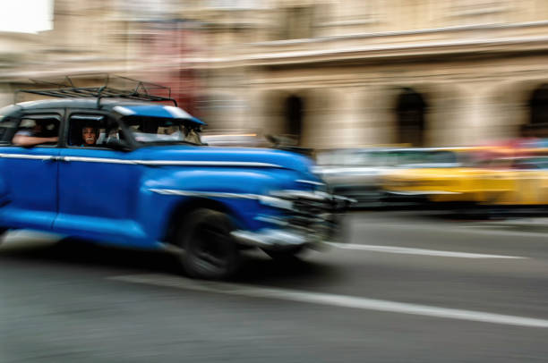 Man looking out of passenger seat of a blue speeding taxi on the street of Havana, Cuba