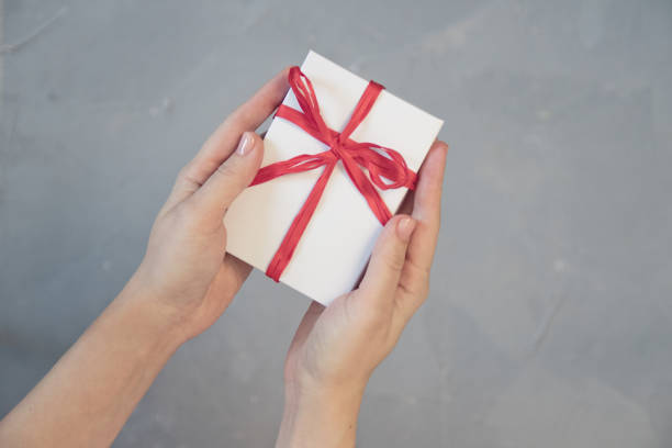 istock Woman hands holding present box with red bow on pastel pink background with multicolored confetti. Flat lay style. 1076707306