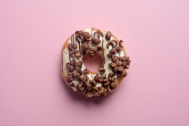 istock Fresh chocolate donut or doughnut decorated wit chocolate cereal on pink pastel table top 1076711596