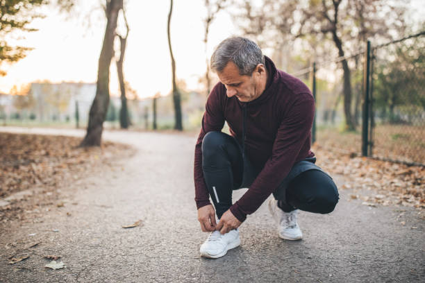 istock Senior man taking pause from jogging to tie his shoelace 1076712868