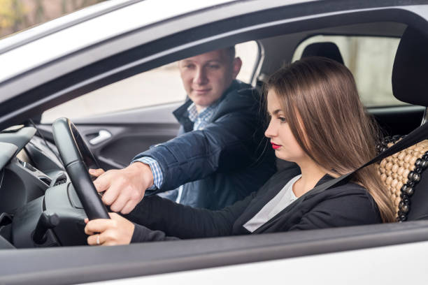 istock Instructor helping young woman drive a car 1076716584