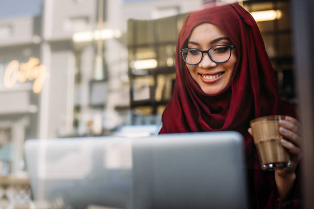 istock Smiling muslim woman using laptop at cafe 1076730334