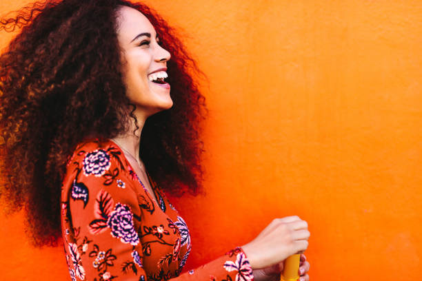 Curly haired woman having fun Side view shot of attractive female with soap bubbles. Young woman having fun against orange background. sundress stock pictures, royalty-free photos & images