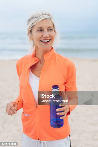 Blond Woman Exercising On A Beach Carrying Water Stock Photo - Download Image Now - 60-69 Years, Active Lifestyle, Adult