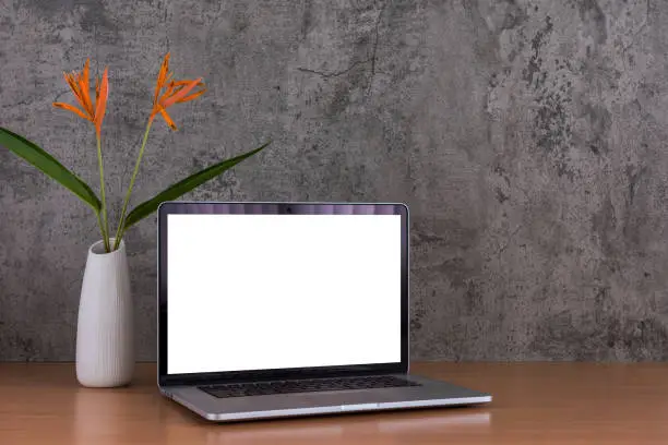 Blank screen of laptop computer with flowers vase on raw concrete background