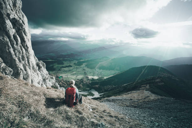 rear view hiking woman with backpack sitting on steep slope on sunny autumn day in mountains