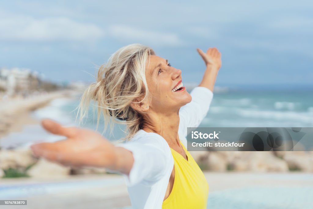 Joyful woman enjoying the freedom of the beach Joyful woman enjoying the freedom of the beach standing with open arms and a happy smile looking up towards the sky Women Stock Photo