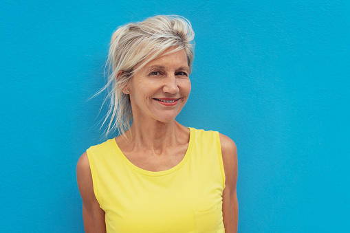 Portrait of smiling mature woman wearing yellow dress posing against blue background