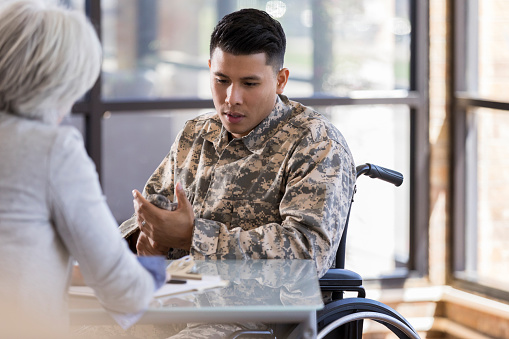 Vulnerable wheelchair-bound male soldier with PTSD discusses hard issues with a caring female mental health professional.