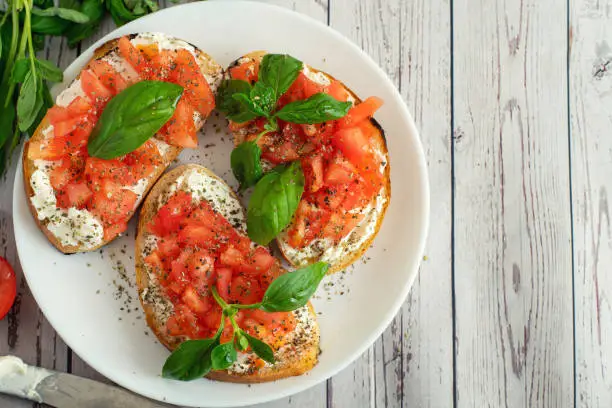 Traditional toasted Italian tomato bruschetta with spice and basil on light wooden background. Top view vith copy space.