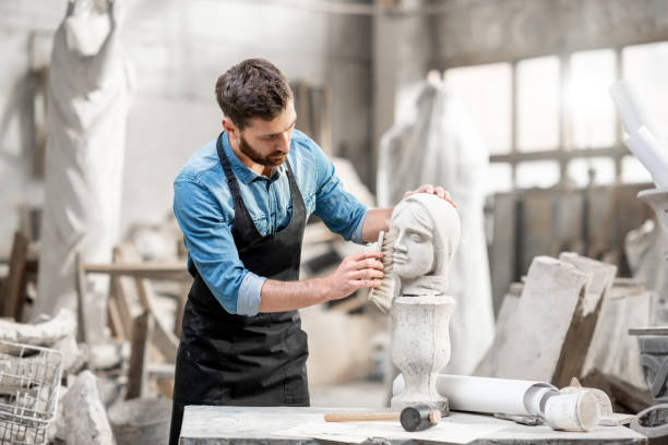 Sculptor working with sculpture in the studio Handsome sculptor brushing stone head sculpture on the table in the atmospheric studio sculpture stock pictures, royalty-free photos & images