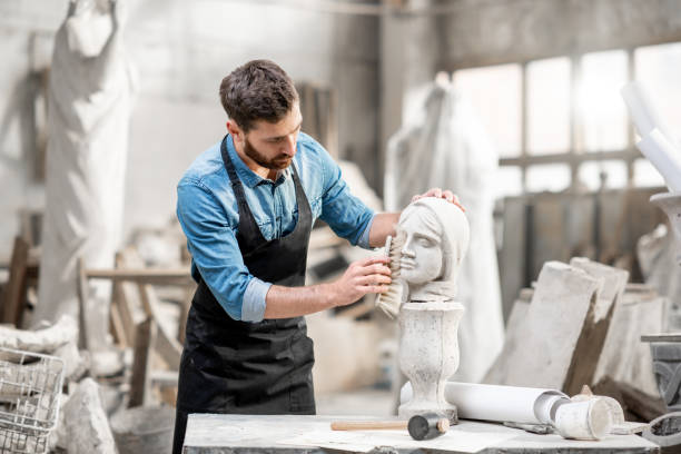 Sculptor working with sculpture in the studio Handsome sculptor brushing stone head sculpture on the table in the atmospheric studio artist sculptor stock pictures, royalty-free photos & images