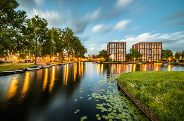 Long exposure of housing buildings and boats along a canal in Amsterdam Dutch canal, lined with houses and boats, with water lilies growing along the sides, in Amsterdam, the Netherlands. dutch architecture stock pictures, royalty-free photos & images