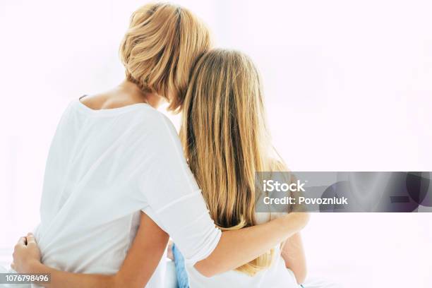 Back View Photo Of Beautiful Young Mother With Her Little Daughter Sitting On The Bed On White Window Backround Stock Photo - Download Image Now