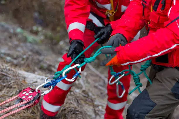 Paramedics from mountain rescue service provide first aid during a training for saving a person in accident in the forest. Unrecognizable people witj ropes and carabiners.