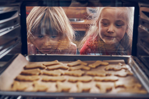 little girls waiting for christmas cookies to bake in the oven - oven imagens e fotografias de stock