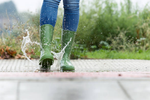 Woman in green rubber boots jumping on the puddle water in the street. Close-up of woman in green rubber boots jumping on the puddle water in the street. rubber boot stock pictures, royalty-free photos & images