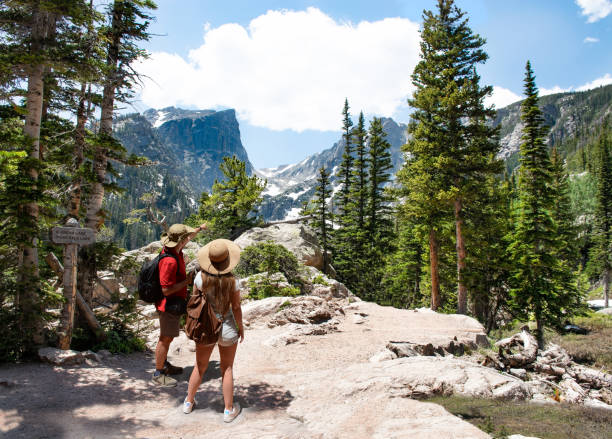 Couple relaxing and enjoying beautiful mountain view in Colorado. Couple relaxing and enjoying beautiful mountain view. Man and woman with backpacks hiking on Emerald Lake trail.Early summer landscape with snow covered mountains.Rocky Mountains National Park, USA hallett peak stock pictures, royalty-free photos & images