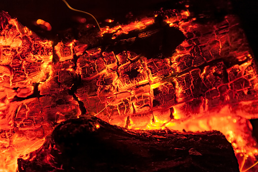 Burning log of wood close-up as abstract background. The hot embers of burning wood log fire. Firewood burning on grill. Texture fire bonfire embers. Smoldering fire