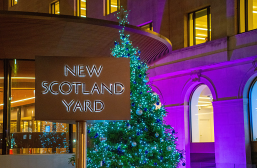 New Scotland Yard sign at night with a Christmas tree in the background.