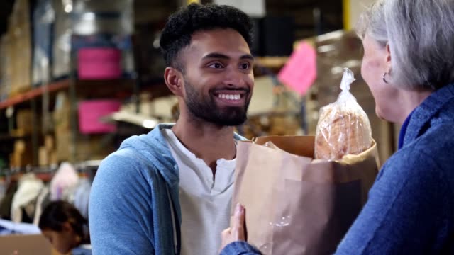 A young male volunteer hands groceries to senior woman