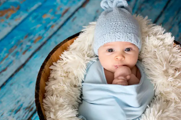 Photo of Little baby boy with knitted hat in a basket, happily smiling