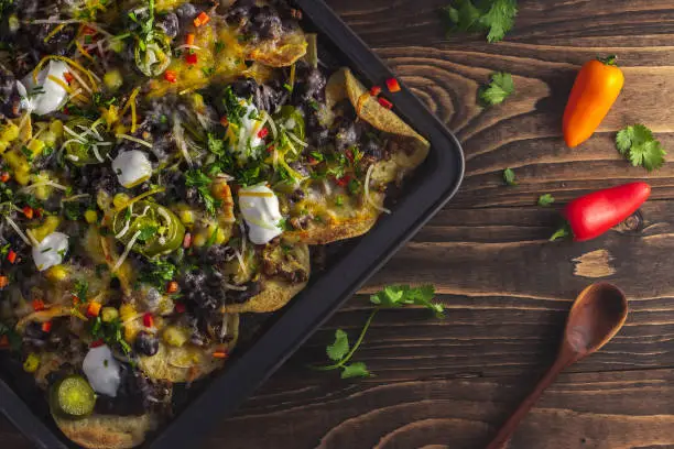 Top view baked pan of nachos with beef, cheese, black beans, peppers, jalapenos