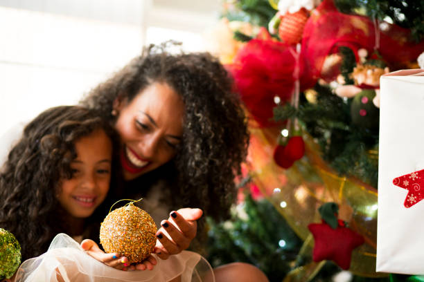 Mom and daughter holding the balls of the Christmas tree, decorating together the Christmas of the house, smiling and enjoying together the intimate moment