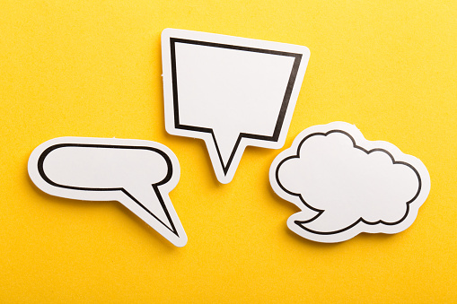 Two hands are holding two speech bubbles which are white and yellow in front of blue background.