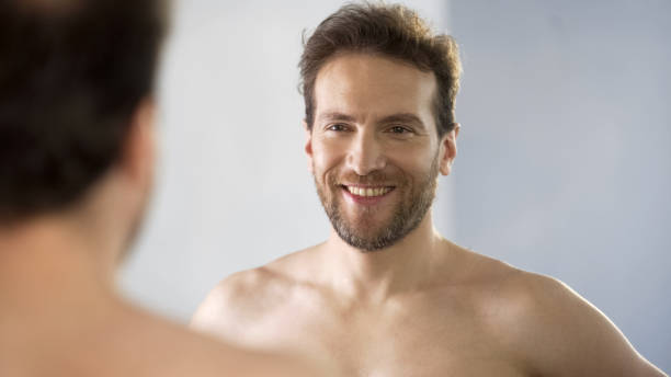 istock Smiling middle-aged man admiringly looking at his reflection in mirror 1076946420