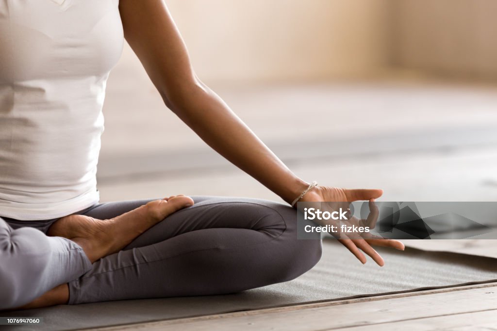 Yogi black woman practicing yoga lesson, doing Ardha Padmasana exercise Yogi black woman practicing yoga lesson, breathing, meditating, doing Ardha Padmasana exercise, Half Lotus pose with mudra gesture, working out, indoor close up. Well being, wellness concept Yoga Stock Photo