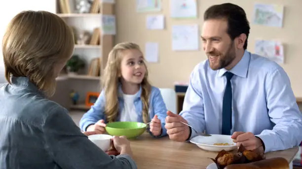 Pretty joyful daughter listening parents during breakfast, family tradition