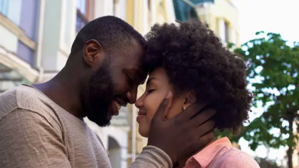 Smiling african couple nuzzling, loving couple hugging, outdoor romantic date