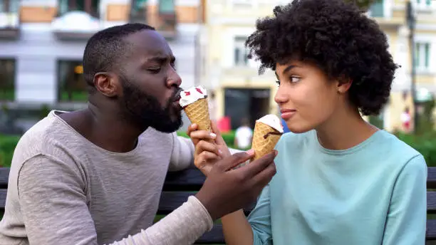 Love partners sharing ice-cream during summer date in city park, fun together