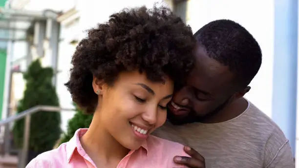 Afro-american couple enjoying date, girl feeling safe in boyfriend arms, smiling