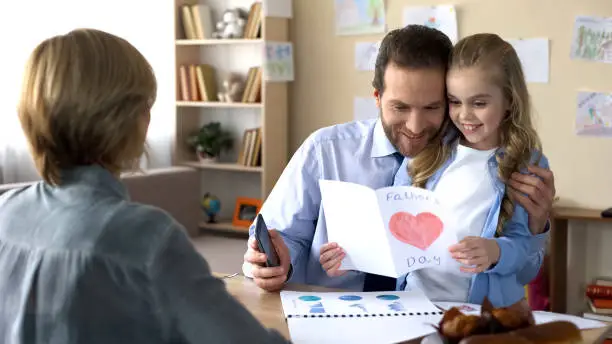 Busy father stopping phone conversation to look at daughters greeting card