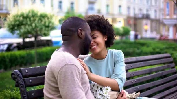 Afro-american loving couple nuzzling on bench, enjoying summer day together