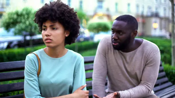 Young man talking to offended girlfriend on bench, jealous woman, break up