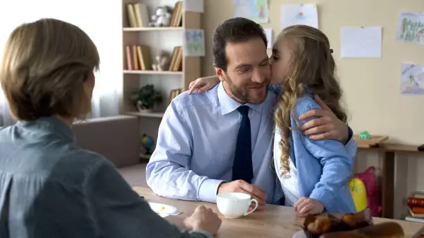 Beautiful female kid kissing loving father at kitchen, family conversation