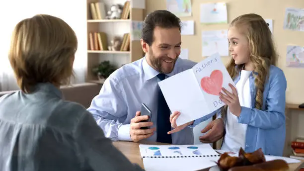 Girl presenting greeting card to busy father, paternal love, family harmony