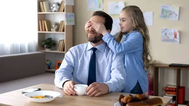 Cute little daughter playing with father in guess who game, family having fun