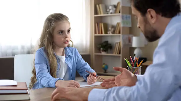 Demanding father making his little daughter doing homework, home schooling