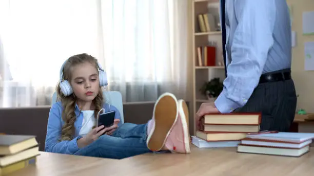 Disobedient girl in headphones listening to music on smartphone, ignoring dad