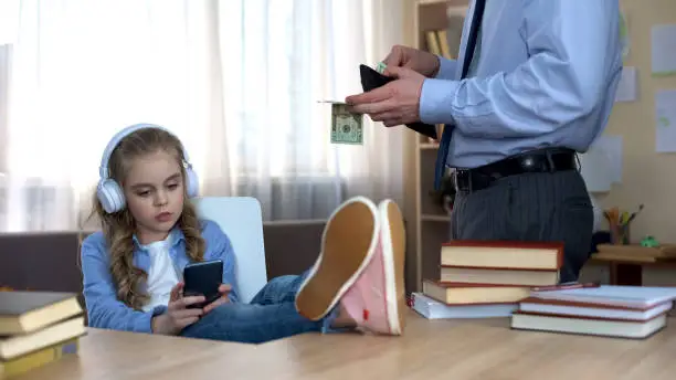 Father in suit giving pocket money to daughter listening to music in headphones