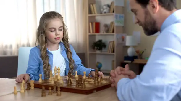 Caring father teaching his little daughter playing chess, family pastime, hobby