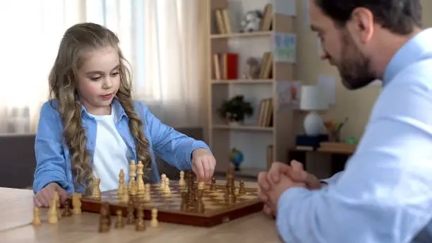 Little daughter thinking over next move, playing chess with father, strategy